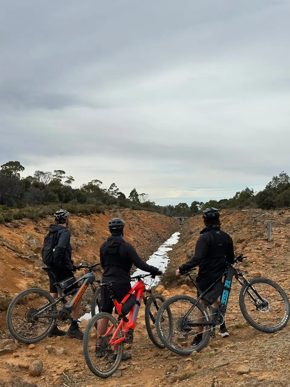 Three riders with their Roar bikes beside a rocky channel in Tasmania